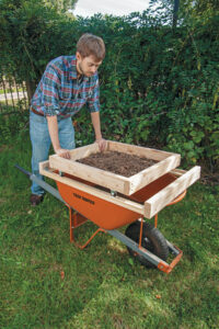 man pushing a soil sifter mounted on to a wheelbarrow